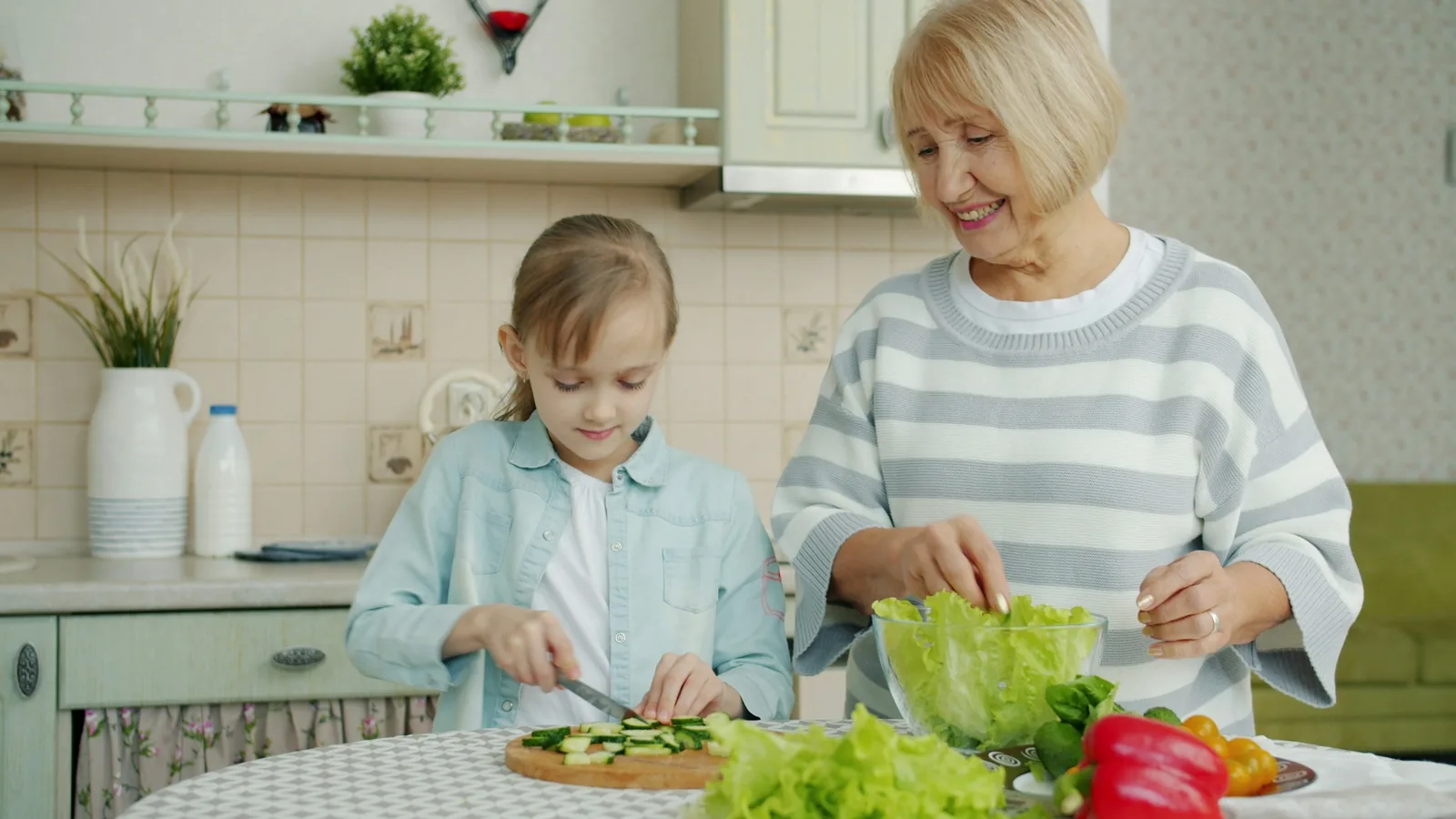 A grandmother and granddaughter preparing vegetables together in a kitchen.