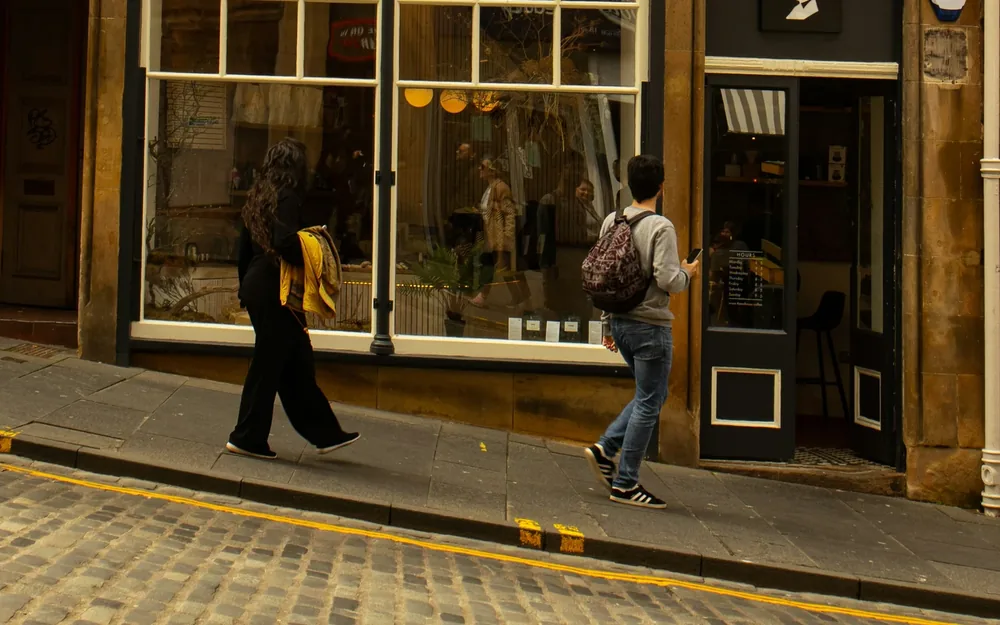 Two people walking past a café window on a cobbled Edinburgh street.