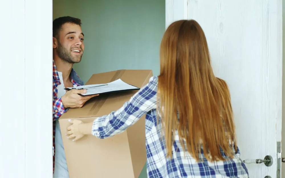 A couple carrying a moving box through an open doorway.
