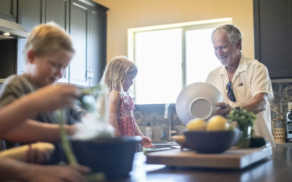 A grandfather and two grandchildren preparing food in a kitchen.